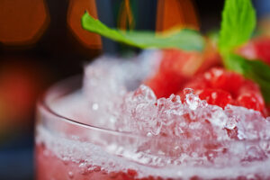 Nahaufnahme eines erfrischenden roten Cocktails mit zerstoßenem Eis, frischen Himbeeren und einem Minzblatt, ideal für GustoFino. Idee für Longdrinks für Hochzeit.