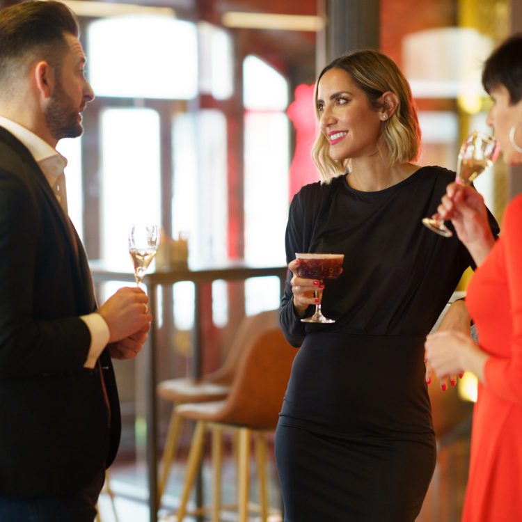 Company of elegant friends gathering in bar Group of well dressed friends drinking alcohol beverages and enjoying meeting while standing at wooden counter in bar with bartender