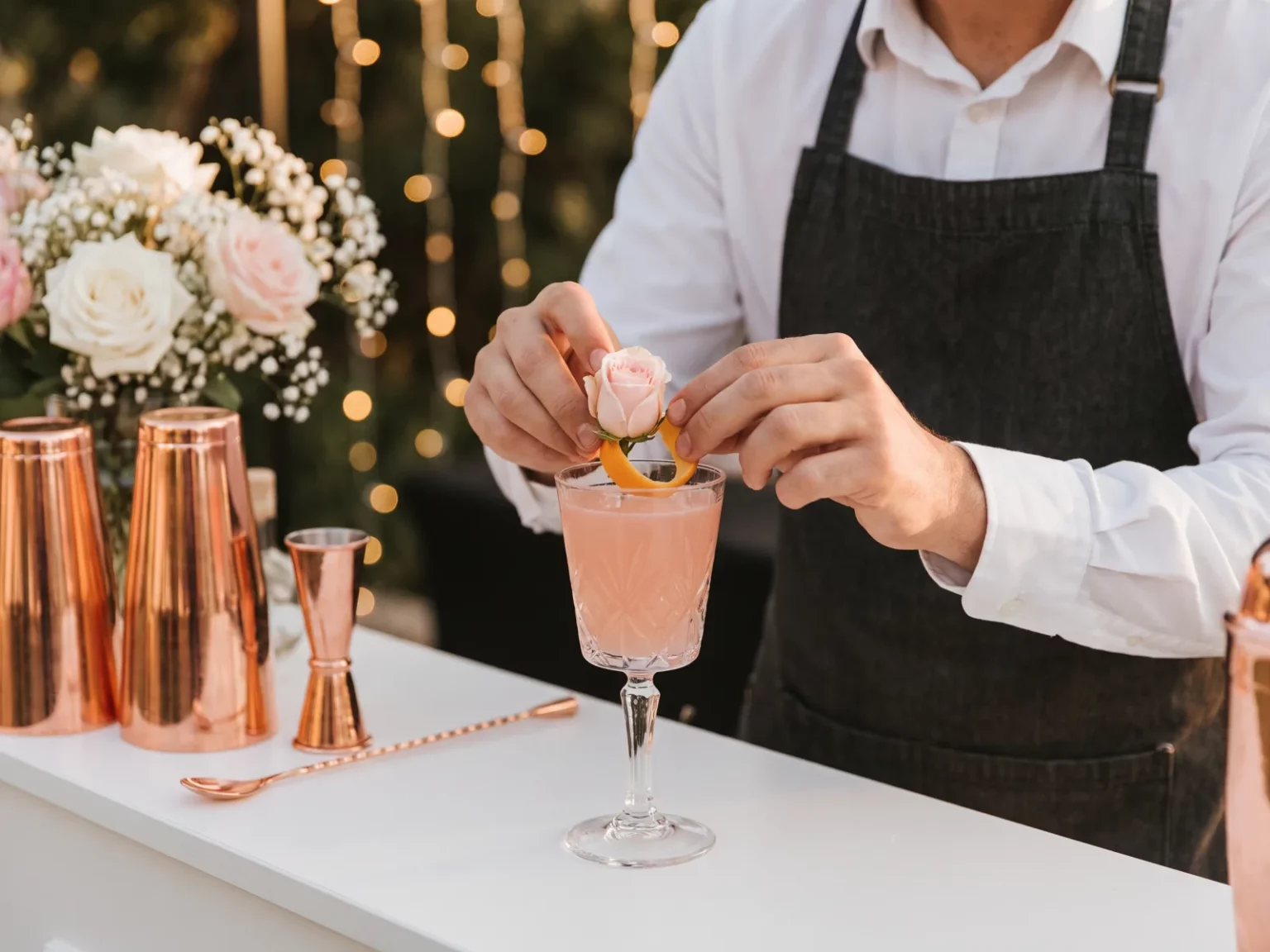Bartender garniert eleganten pinken Cocktail mit Rosenblüte und Orangenzeste für eine Partyservice Geburtstagsfeier.